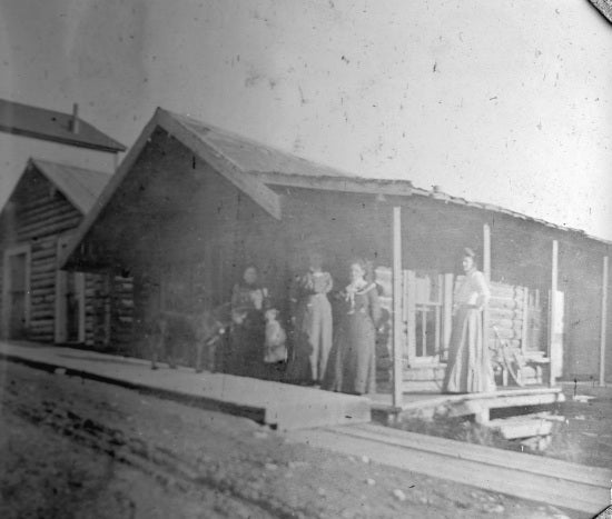 Four woman and child on porch of log cabin, c1902
